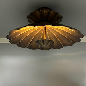 May include: A flush mount ceiling light fixture with a dark bronze finish. The fixture features a large, scalloped, shell-shaped shade with a smaller, matching scalloped element suspended from the center by a thin, vertical metal rod.