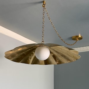 May include: A brass-colored, seashell-shaped pendant light fixture with a white globe bulb. The light hangs from a chain and is mounted to the ceiling. The fixture has a textured surface and a decorative design.