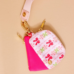 May include: A pink and white floral print coin purse with a gold zipper and hardware. The purse has a pink strap and a gold clasp. The text "alpha omicron pi" is printed on the purse.