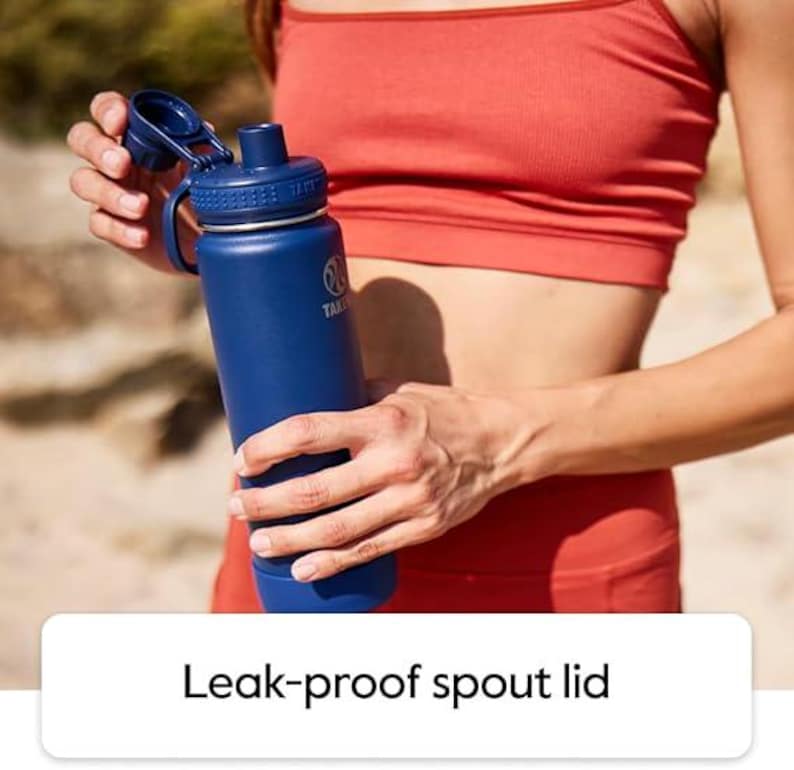 Pode incluir: Uma garrafa de &aacute;gua azul isolada com tampa de bico &agrave; prova de vazamentos. A garrafa &eacute; segurada por uma pessoa vestindo um suti&atilde; esportivo e leggings vermelhos. A garrafa tem uma al&ccedil;a e um logotipo. O texto "Leak-proof spout lid" est&aacute; na parte inferior.