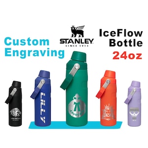 Pode incluir: Uma coleção de garrafas Stanley IceFlow em várias cores, incluindo preto, azul, verde, laranja e roxo. Cada garrafa apresenta uma alça prateada e uma gravação personalizada. O texto "Custom Engraving" e "IceFlow Bottle 24oz" é exibido.