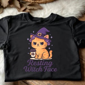 May include: Black t-shirt featuring a cartoon cat with an orange and brown striped pattern, wearing a purple witch hat and holding a coffee cup. The text "Resting Witch Face" is below the cat.