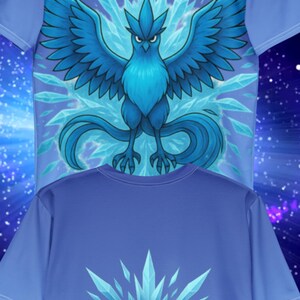 K&ouml;nnte beinhalten: Zwei blaue T-Shirts. Das obere Shirt zeigt eine detaillierte Illustration eines blauen Vogels mit ausgebreiteten Fl&uuml;geln, umgeben von Eiskristallen. Das untere Shirt zeigt das Wort "MYSTIC" in einer stilisierten Schriftart, ebenfalls mit Eiskristall-Akzenten.