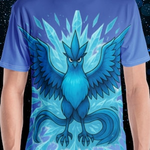 K&ouml;nnte beinhalten: Blaues T-Shirt mit einem stilisierten blauen Vogel mit ausgebreiteten Fl&uuml;geln und langem Schwanz, vor einem Hintergrund aus Eiskristallen. Der Vogel hat einen strengen Ausdruck. Das Shirt ist einfarbig blau.
