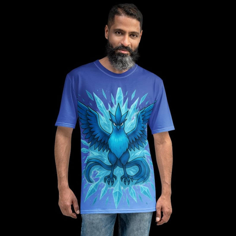 K&ouml;nnte beinhalten: Blaues T-Shirt mit einem stilisierten blauen Vogel mit ausgebreiteten Fl&uuml;geln, umgeben von Eiskristallen. Der Vogel hat einen strengen Ausdruck. Das T-Shirt ist einfarbig blau.