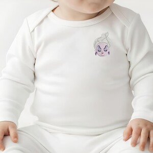 May include: A long-sleeved white baby bodysuit featuring a small embroidered graphic on the upper left chest. The graphic depicts the face of a character with pale skin, white hair, purple earrings, and a stern expression with closed eyes.