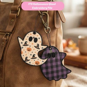 May include: Two ghost-shaped embroidered bag charms attached to a metal lobster clasp. One ghost features a cream background with orange pumpkins, black witch hats, and stars. The other ghost has a purple and black buffalo plaid pattern.
