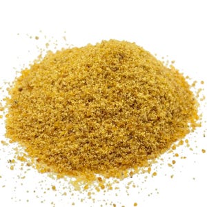 May include: A close-up shot of a pile of fine, light brown granules. The granules have a slightly coarse texture and appear to be a spice or seasoning. The background is plain white, which highlights the color and texture of the granules.