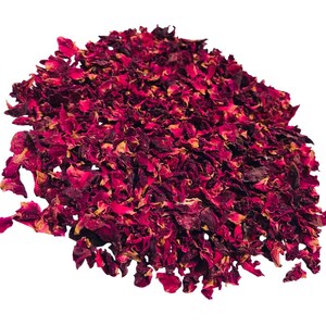 May include: A pile of dried rose petals in shades of deep red and burgundy, with hints of yellow. The petals are irregularly shaped and appear to be slightly curled, creating a textured appearance. The background is plain white.