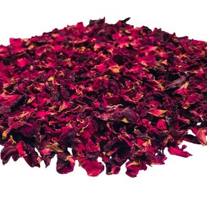 May include: A pile of dried rose petals, predominantly deep red with hints of yellow and brown. The petals are irregularly shaped and appear to be of varying sizes. The background is plain white, highlighting the natural colors of the petals.