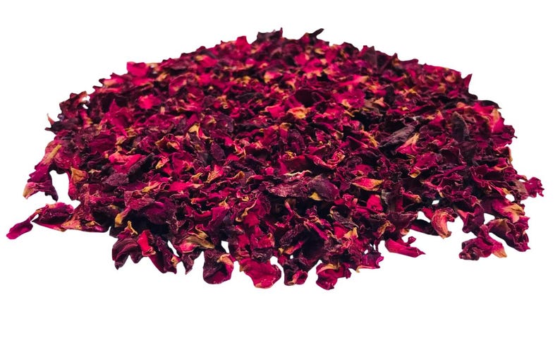 May include: A pile of dried rose petals, predominantly deep red with hints of yellow and brown. The petals are irregularly shaped and appear to be of varying sizes. The background is plain white, highlighting the natural colors of the petals.