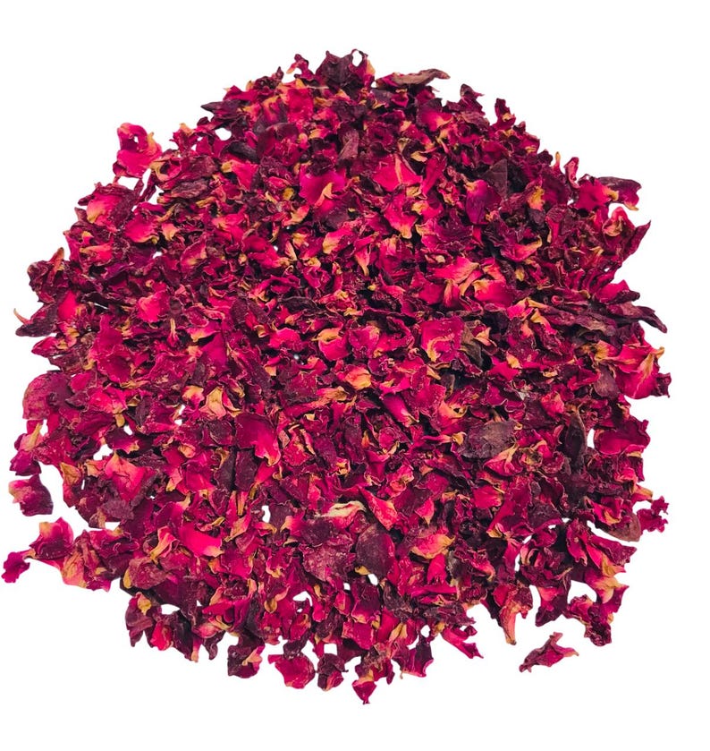 May include: A pile of dried rose petals in shades of deep red and burgundy, with hints of yellow and brown. The petals are irregularly shaped and appear to be loose, creating a textured surface. The image is set against a plain white background.