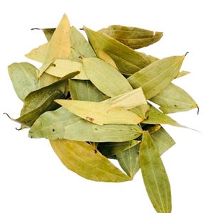 Op de afbeelding: Een stapel gedroogde laurierbladeren, met een mix van groen- en geelbruine tinten. De bladeren zijn langwerpig en hebben een licht getextureerd oppervlak, met zichtbare nerven. De afbeelding is tegen een witte achtergrond.