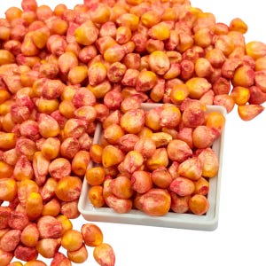 Könnte beinhalten: Nahaufnahme eines Haufens orangefarbener und roter Maiskörner. Die Körner befinden sich in einer weißen Schale und sind darum herum verstreut. Die Körner haben eine glatte Textur und sind eine Mischung aus Orange und Rot.