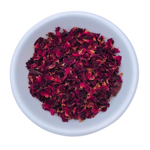 May include: A white ceramic bowl filled with dried rose petals. The petals are a deep burgundy color with hints of yellow and orange. The bowl is round and has a simple, clean design.