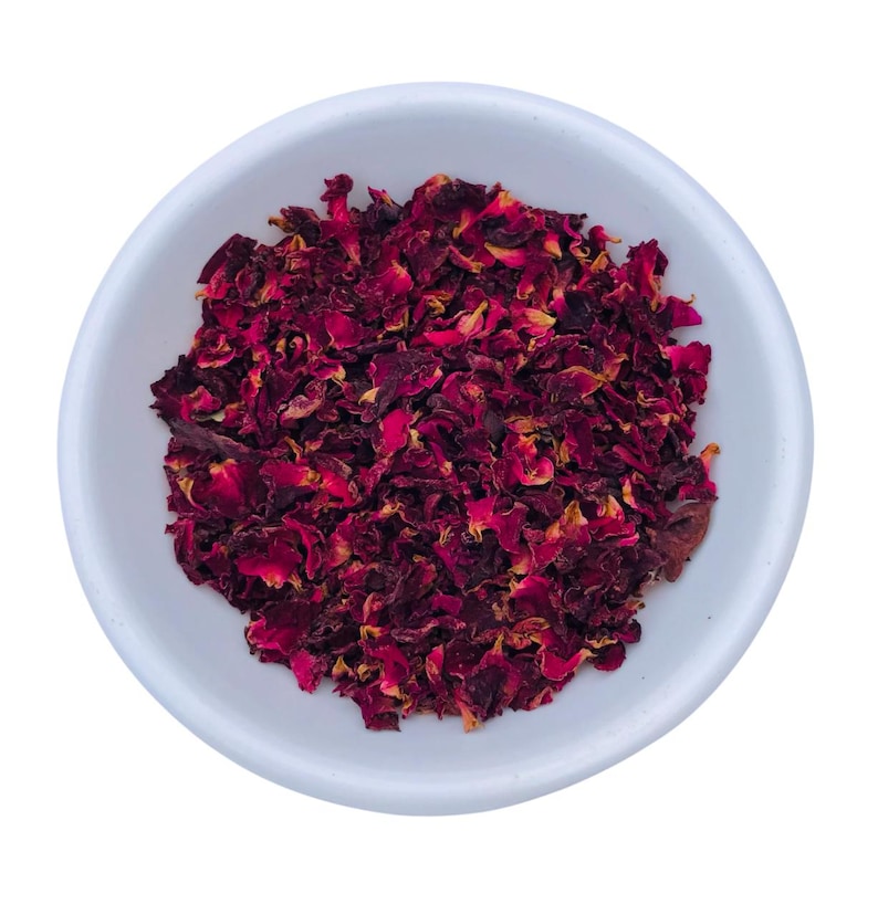 May include: A white ceramic bowl filled with dried rose petals. The petals are a deep burgundy color with hints of yellow and orange. The bowl is round and has a simple, clean design.