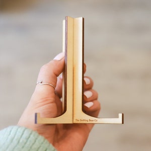 Könnte beinhalten: Ein Holzständer zum Ausstellen von Fotos oder kleinen Gegenständen. Der Ständer ist aus hellbraunem Holz gefertigt und hat ein schlichtes Design. Der Ständer ist mit "The Drifting Bear Co." beschriftet.