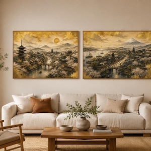 以下が含まれることがあります： 金色の色調で描かれた日本の風景画の長方形の壁掛けアート2枚。パゴダ、桜の木、川、遠くの山の頂上が輝く太陽の下に描かれており、薄い木製のフレームに入れられ、ベージュの布製ソファの上に飾られています。