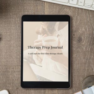 Peut inclure: Une tablette noire affichant le texte "Therapy Prep Journal" et "A soft start for first-time therapy clients." La tablette est posée sur une surface en bois, avec un clavier, un téléphone et une loupe en arrière-plan.
