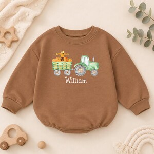 May include: A brown long-sleeve crewneck sweatshirt featuring a watercolor-style graphic of a green tractor pulling a wagon filled with orange pumpkins and a scarecrow. The name William is printed in white text below the tractor graphic.