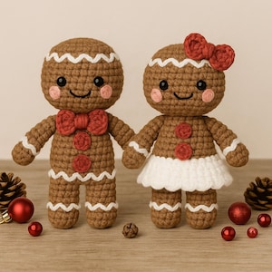 May include: Two handmade crochet gingerbread people, one with a bow tie and the other with a bow, stand side-by-side. They have white icing details, rosy cheeks, and red button accents. The background includes Christmas ornaments and pinecones.