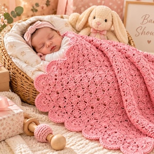 Peut inclure: Une couverture pour bébé en crochet rose avec un bord festonné drapée sur un panier en osier contenant un nourrisson endormi portant un bandeau rose, avec une peluche lapin et un panneau indiquant Baby Shower.