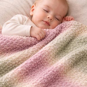 Könnte beinhalten: Ein schlafendes Baby liegt unter einer weichen, gestrickten Decke. Die Decke hat einen Farbverlauf von Rosa über Creme bis Grün. Das Baby trägt einen weißen Langarm-Body.