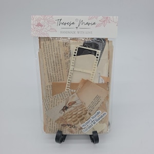May include: A clear plastic bag filled with vintage paper ephemera, including book pages, film strips, and aged paper scraps. The bag is labeled "Mystery Bundle Curated at Random" and "Theresa Maria Handmade with Love."