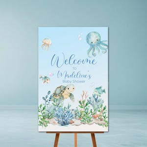 May include: A baby shower welcome sign featuring watercolor illustrations of sea creatures, including an octopus, turtle, and fish. The sign reads "Welcome to Madeline's Baby Shower" in elegant script against a light blue background.