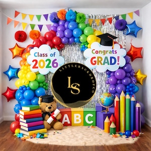 Puede incluir: Un telón de fondo con temática de graduación con globos coloridos, decoraciones en forma de estrella y los textos "Class of 2026" y "Congrats GRAD!". Incluye un oso de peluche, libros y bloques ABC.