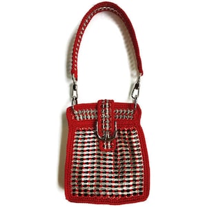 Peut inclure: Un sac à main rouge en crochet avec une boucle argentée et une bandoulière en chaîne. Le sac est fabriqué à partir de matériaux recyclés.