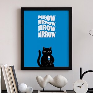 May include: A framed art print featuring a black cat holding a wine glass, set against a vibrant blue background. The print includes the words "MEOW MRROW MROW MRROW" in white, stylized lettering. The artwork is displayed on a shelf with decorative items.