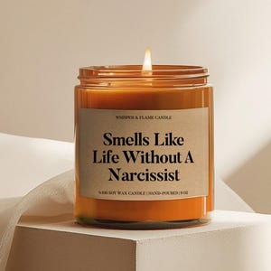 May include: An orange candle in a glass jar with a label saying "Smells Like Life Without A Narcissist." The candle is hand-poured and made with soy wax. The jar is 539 grams.