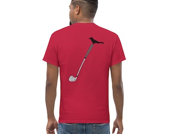 May include: A red short-sleeved t-shirt featuring a graphic on the back. The graphic depicts a black bird perched on the handle of a silver golf club. The shirt is worn with blue denim jeans, showing the back view of the garment and the design.