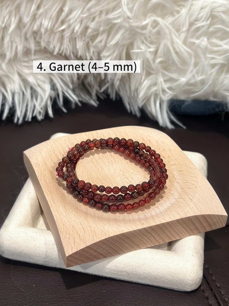 May include: A set of three garnet bead bracelets, each with 4-5 mm beads, displayed on a light wooden stand. The beads are a deep reddish-brown color. The text "4. Garnet (4-5 mm)" is visible in the image.