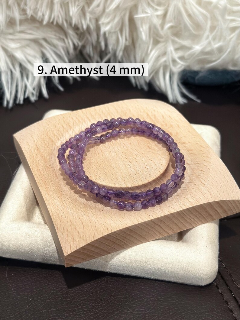 May include: A pair of amethyst bracelets, each composed of small, round, purple beads, are displayed on a light-colored wooden block. The bracelets are approximately 4 mm in diameter. The text "9. Amethyst (4 mm)" is visible in the image.