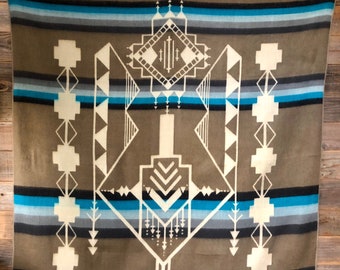 May include: A brown and blue patterned woven blanket with a geometric design. The blanket has a white label with the text "KOU CANVAS" in the bottom right corner.