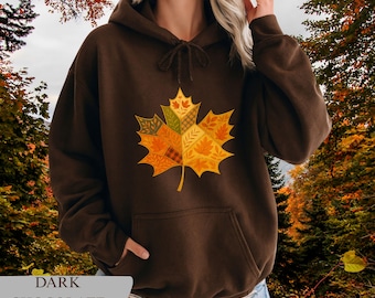 May include: Dark chocolate brown hoodie with a large, colorful maple leaf design on the front. The leaf is composed of various autumn-themed patterns and colors. The text "DARK CHOCOLATE" is at the bottom.