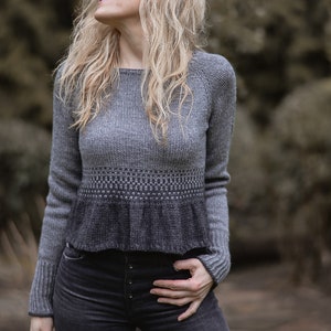 May include: A gray and black knit sweater with a ruffled hem and a textured pattern. The sweater is cropped and has long sleeves.