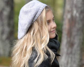May include: A young woman with long blonde hair wearing a gray knitted beret and a black leather jacket. She is standing in a forest setting.