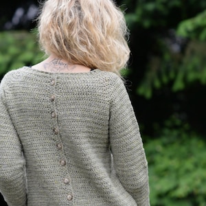 Puede incluir: Un suéter de crochet verde con botones en la espalda.