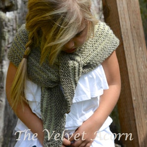 May include: A young person wearing a gray and green striped knitted scarf with a white ruffled top and blue jeans. The scarf is draped over the person's shoulders and tied at the neck. The person is looking down at the scarf.