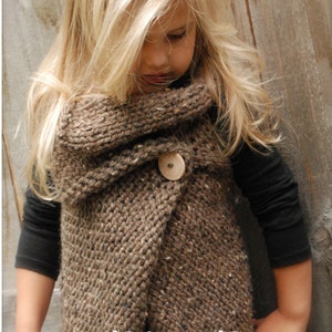 May include: A brown knitted cowl with a wooden button closure. The cowl is worn by a young girl with long blonde hair. The text "PDF Pattern" is visible at the bottom of the image.