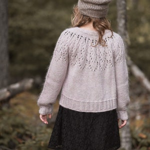 Könnte beinhalten: Ein hellrosa gestrickter Cardigan mit einem zarten Spitzenmuster auf der Rückseite. Der Cardigan hat lange Ärmel und eine lockere Passform.