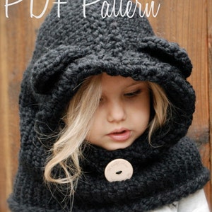 Peut inclure: Une écharpe à capuche en tricot noir avec une fermeture à bouton. La capuche a des rabats d'oreilles et l'écharpe est portée par un enfant.