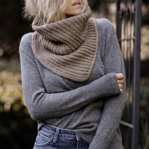 May include: A grey sweater with a brown knitted cowl neck scarf. The scarf is folded over and worn around the neck.