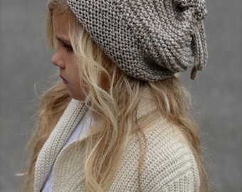May include: A brown and beige knitted beanie with a long tassel. The beanie is slouchy and has a ribbed texture.