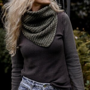 May include: A woman wearing a dark brown long-sleeved shirt with a green and brown knitted scarf. The scarf is tied around her neck and hangs down her chest.