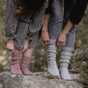 Può includere: Due persone che indossano calze lunghe. Una persona indossa un vestito floreale bianco e nero e calze rosa. L'altra persona indossa jeans e calze grigie.