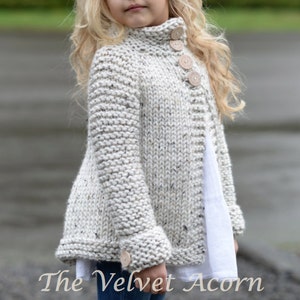 Pu&ograve; includere: Un cardigan di maglia bianco con collo alto e chiusura con bottoni. Il cardigan ha una texture macchiettata e bottoni in legno.